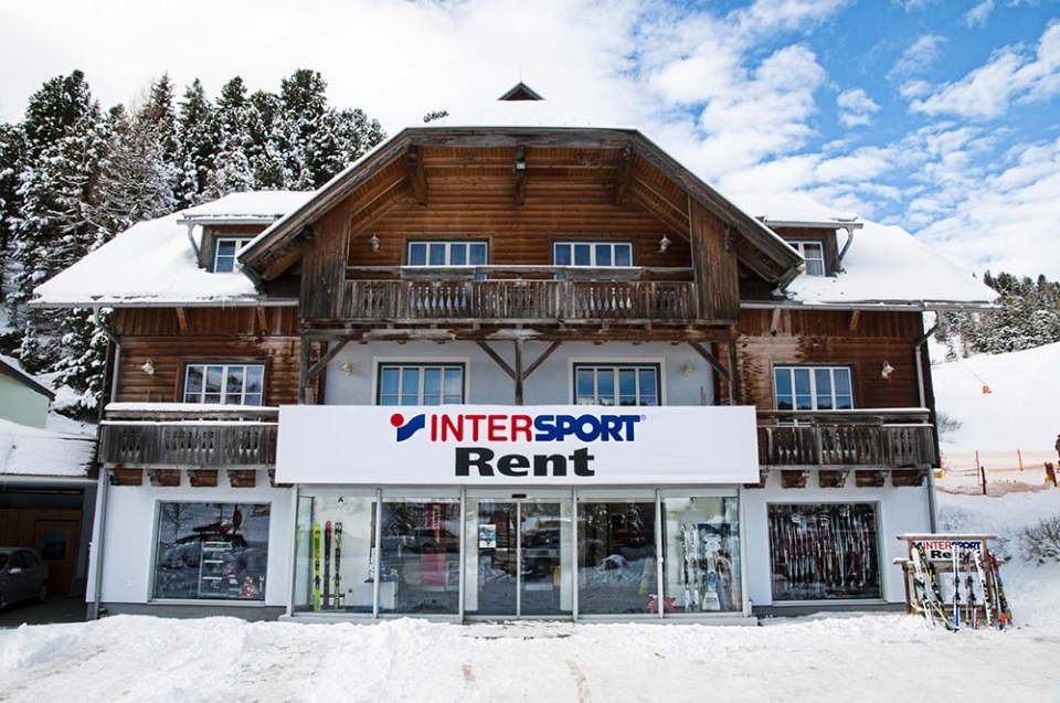 INTERSPORT Rent Shop mit Holzfassade und großen Schild mit INTERSPORT Rent Logo im Winter