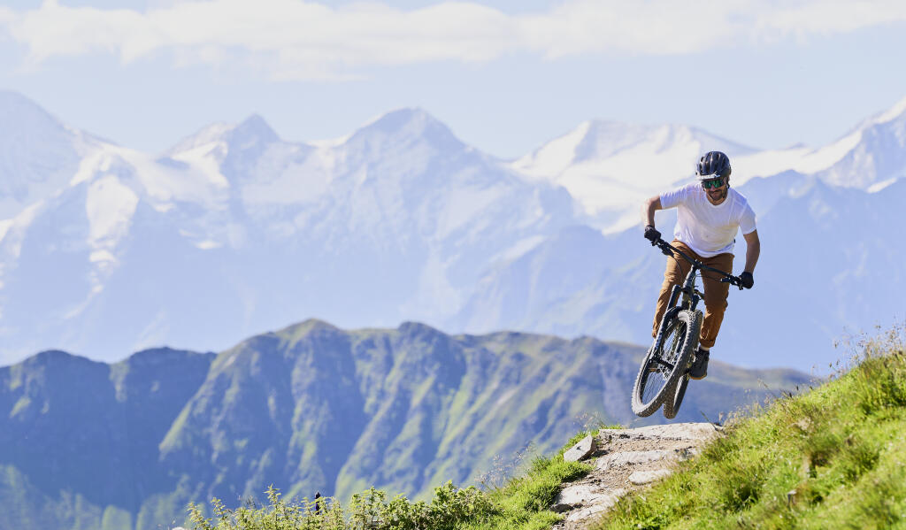 Biker fährt auf einem Trail, im Hintergrund ist die Berglandschaft zu sehen